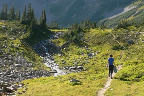 Hiker walking a trail beside a mountain stream